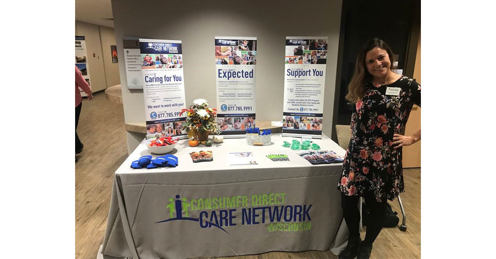 IRIS Supervisor Denise Monroe standing to the right of the Consumer Direct Care Network Wisconsin table at the 13th Annual New Richmond Caregiver Conference.