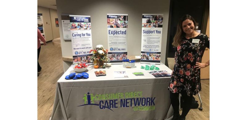 IRIS Supervisor Denise Monroe standing to the right of the Consumer Direct Care Network Wisconsin table at the 13th Annual New Richmond Caregiver Conference.
